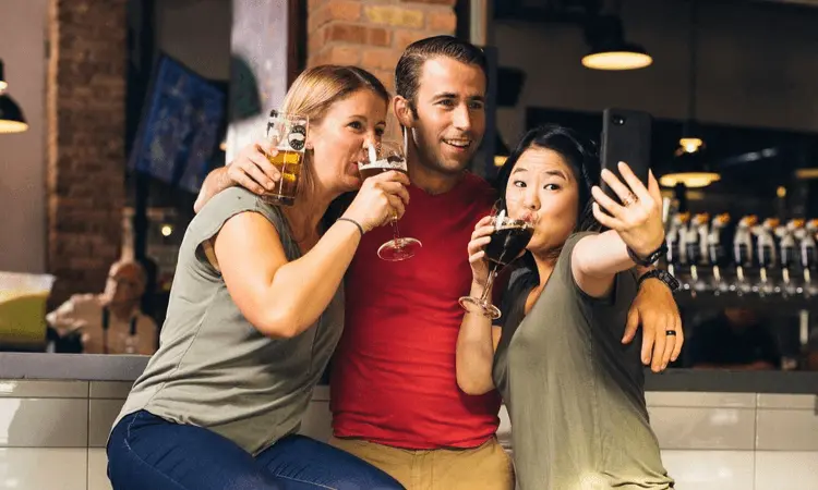 Three friends celebrating Blackout Wednesday at a bar, drinking beer and taking a selfie.