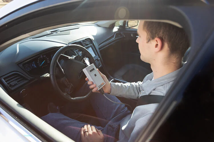 Driver seated in a car holding an ignition interlock device, preparing to take a breath test before starting the vehicle