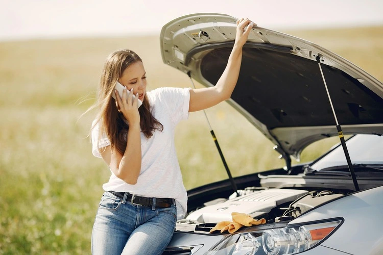 Young woman on the phone standing by her car with the hood open, waiting for Intoxalock roadside assistance