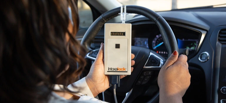 Woman in a car holding an Intoxalock ignition interlock device