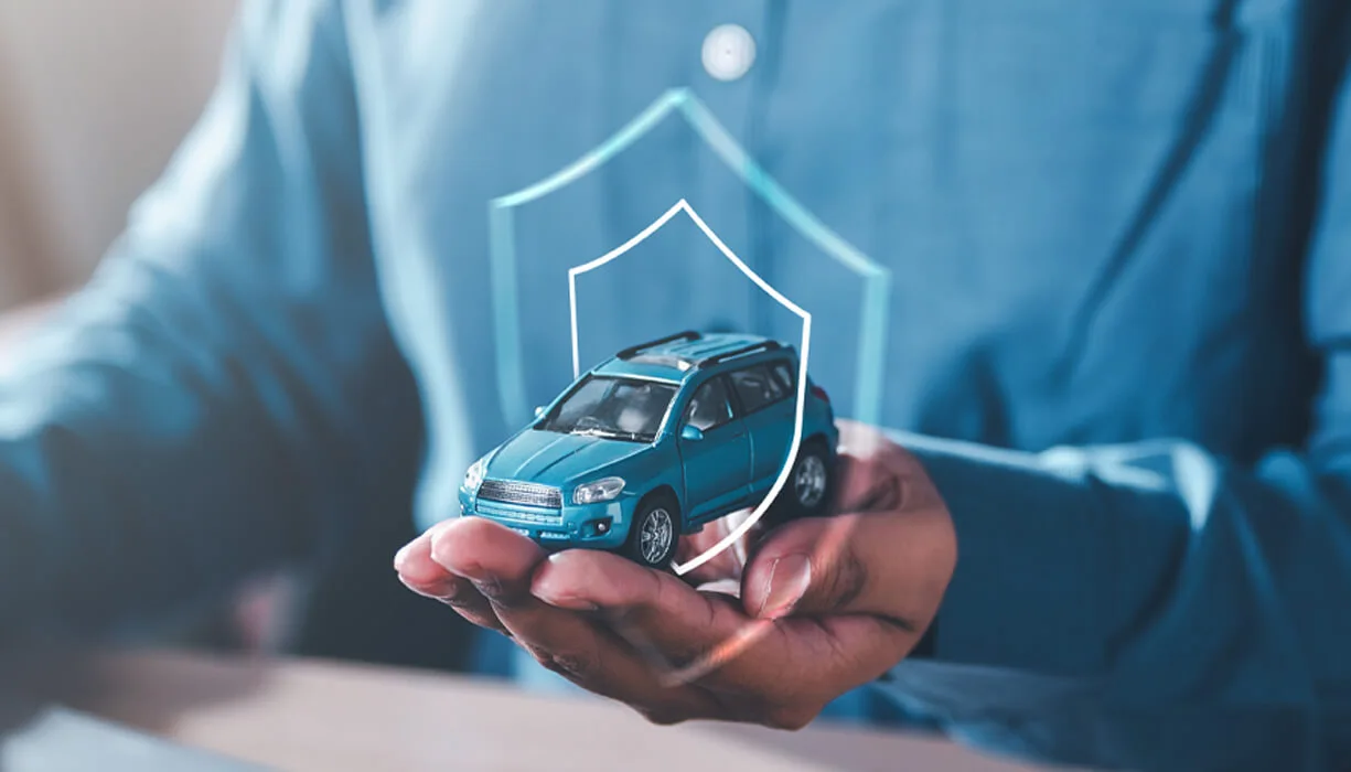 Close-up of a person's hands holding a small blue toy car with a transparent shield symbol overlaid, representing SR-22 coverage for high-risk drivers.