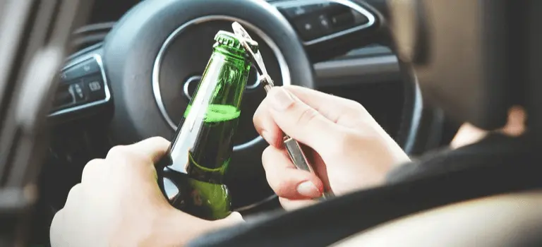 Person holding a beer bottle while sitting in the driver's seat of a car