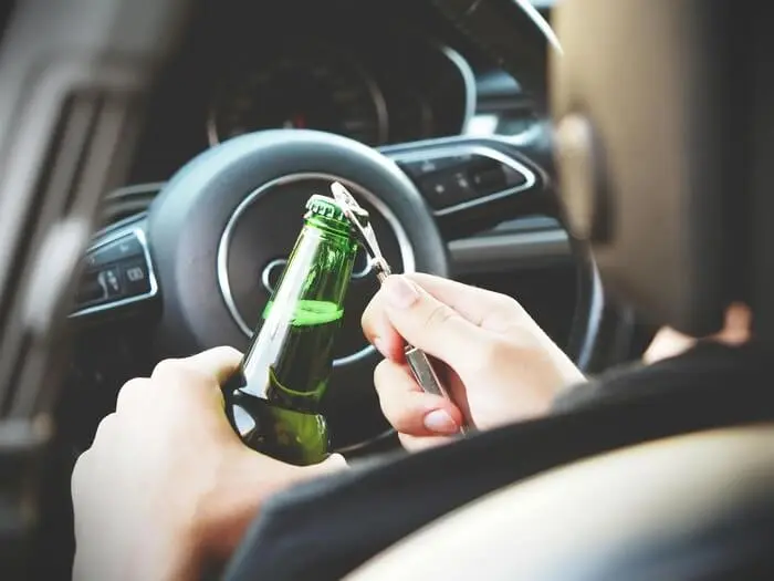 Person holding a beer bottle while sitting in the driver's seat of a car