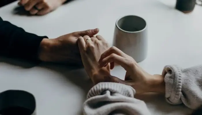 Two people holding hands over a white table with a cup tea next to them
