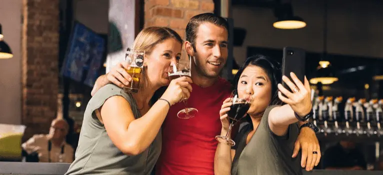 Three friends celebrating Blackout Wednesday at a bar, drinking beer and taking a selfie.