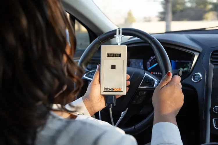 Woman in a car holding an Intoxalock ignition interlock device